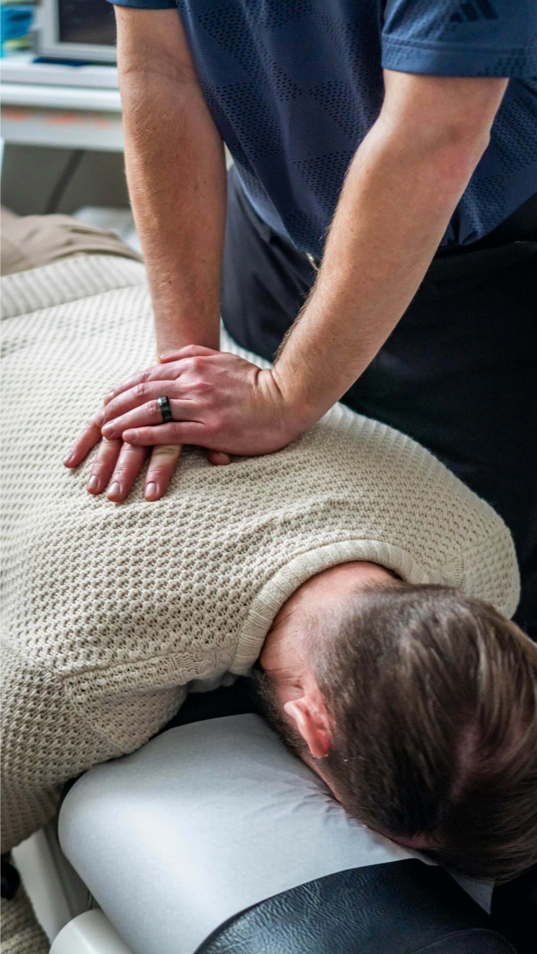A patient lies prone receiving a manual chiropractic adjustment to the middle thoracic region