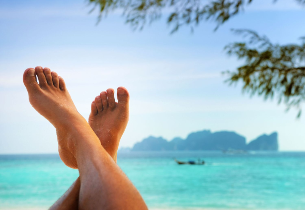 a person's fee are extended and crossed with the ocean in the distance behind.