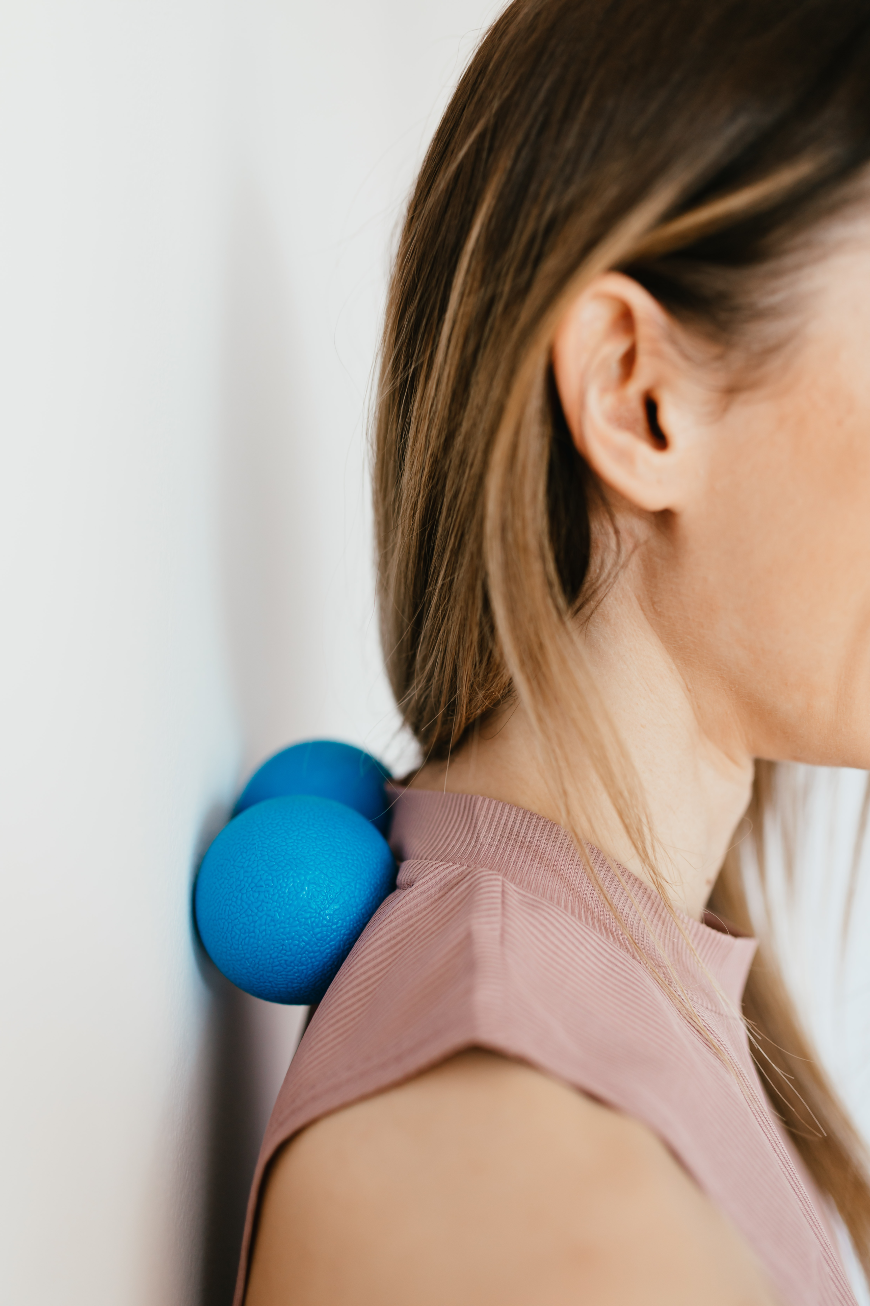 A woman leans against a wall pinning two blue balls between her upper back and the wall